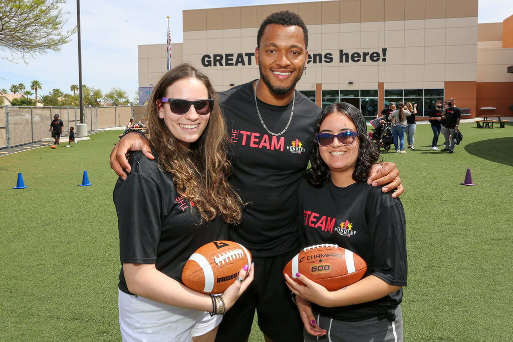 Brett posing with two members of "The Team" who are each holding footballs
