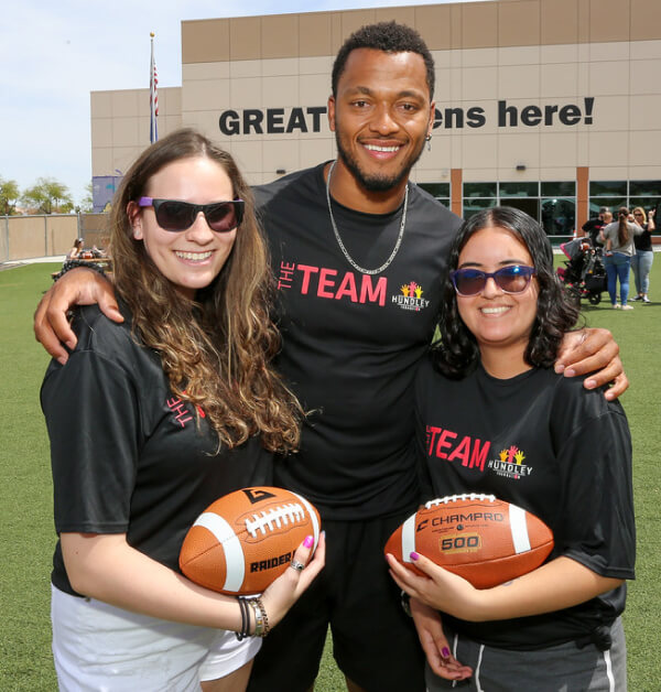 Brett posing with a couple members of "The Team" who are each holding footballs